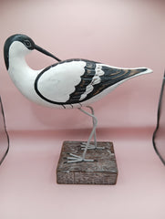 Hand-carved wooden avocet bird sculptures with black and white detailing on rustic stands