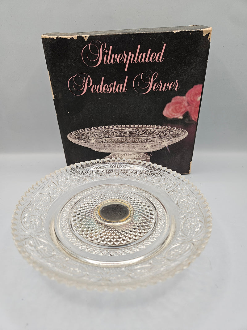 A close-up view of a silver-plated crystal pedestal server, featuring a luxurious combination of silver and crystal. The server measures 5.75"W x 1.5"H and is presented in its original packaging, perfect for serving or as a decorative item