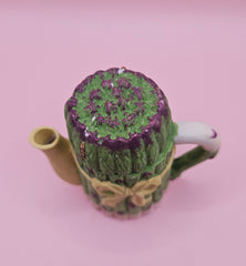 Vintage ceramic miniature teapot shaped like asparagus stalks with purple tips and a yellow ribbon bow, approximately 3.6 inches tall.