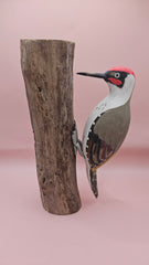 Three individual hand-painted woodpecker figures mounted on varying pieces of natural wood displayed on a teal tabletop.