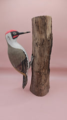 Three individual hand-painted woodpecker figures mounted on varying pieces of natural wood displayed on a teal tabletop.