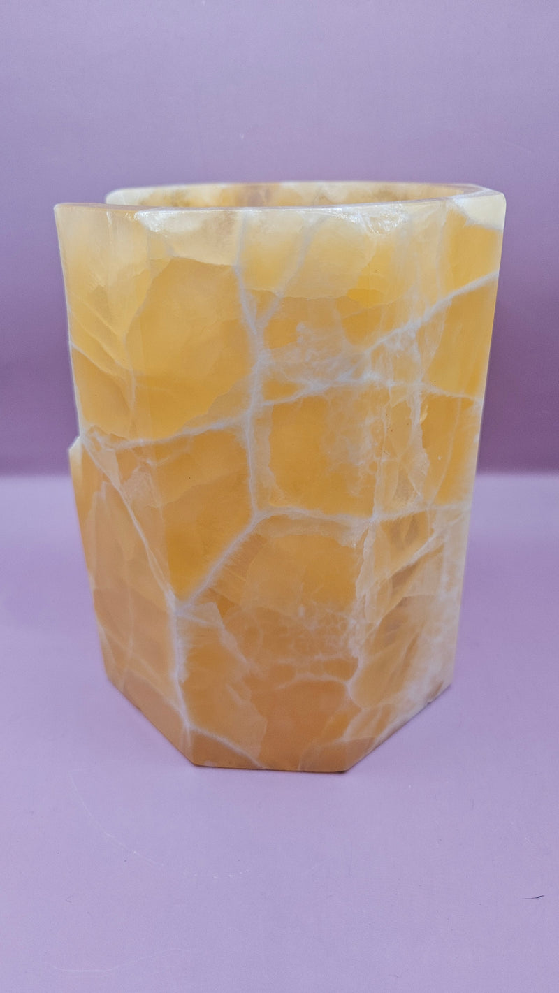 Honeycomb calcite candle cover with translucent golden tones and a hexagonal shape, measuring 6.75x5.5 inches.