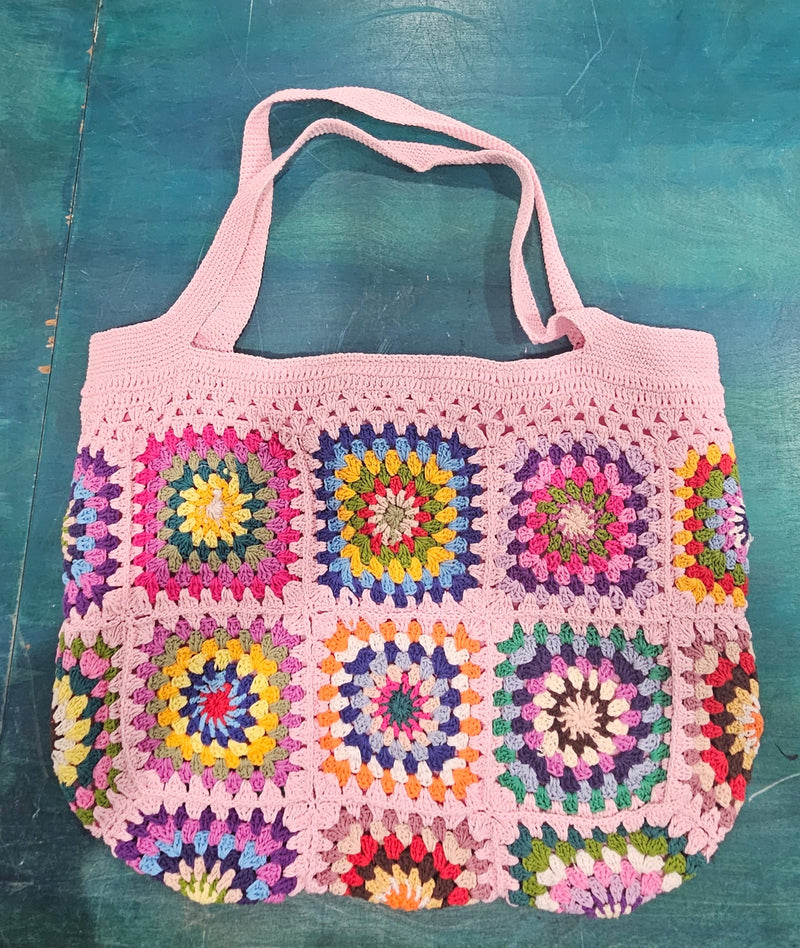 colorful handmade crochet tote bags with granny square designs in pink and black, tan and blue backgrounds, displayed on a teal surface