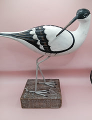 Hand-carved wooden avocet bird sculptures with black and white detailing on rustic stands