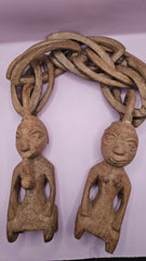 Vintage African hand-carved wooden wedding chain featuring two carved figures connected by a wooden chain on a pink background.