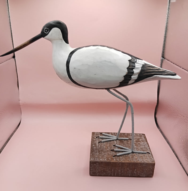 Hand-carved wooden avocet bird sculptures with black and white detailing on rustic stands
