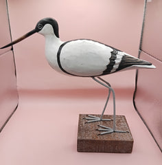 Hand-carved wooden avocet bird sculptures with black and white detailing on rustic stands