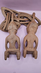 Vintage African hand-carved wooden wedding chain featuring two carved figures connected by a wooden chain on a pink background.