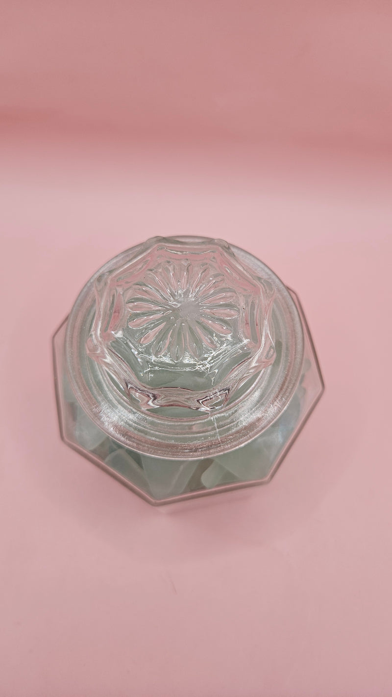 Hexagonal glass jar with lid filled with frosted aqua sea glass, coastal home decor accent on pink background