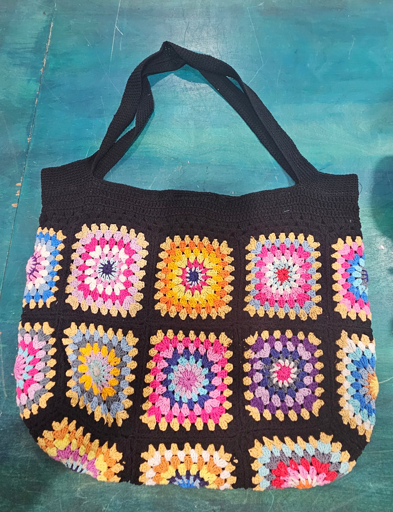 colorful handmade crochet tote bags with granny square designs in pink and black, tan and blue backgrounds, displayed on a teal surface