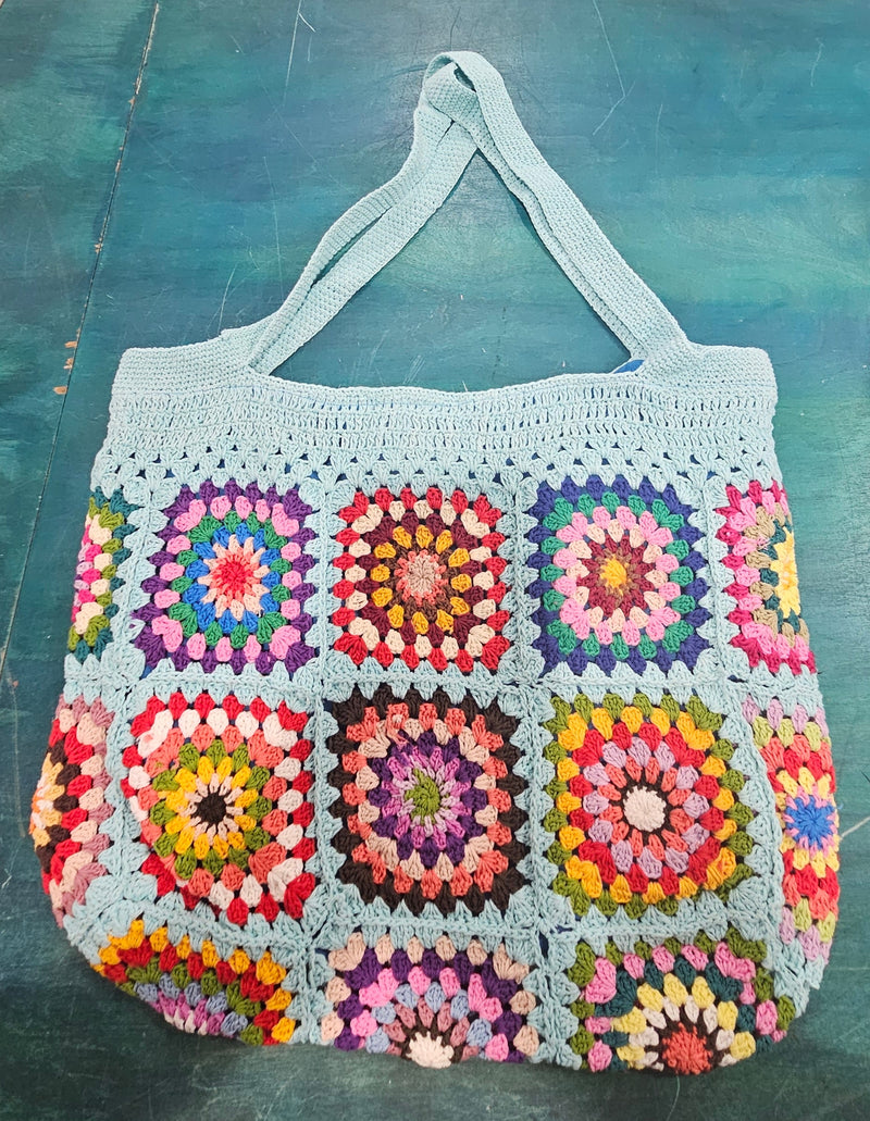 colorful handmade crochet tote bags with granny square designs in pink and black, tan and blue backgrounds, displayed on a teal surface