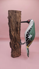 Three individual hand-painted woodpecker figures mounted on varying pieces of natural wood displayed on a teal tabletop.