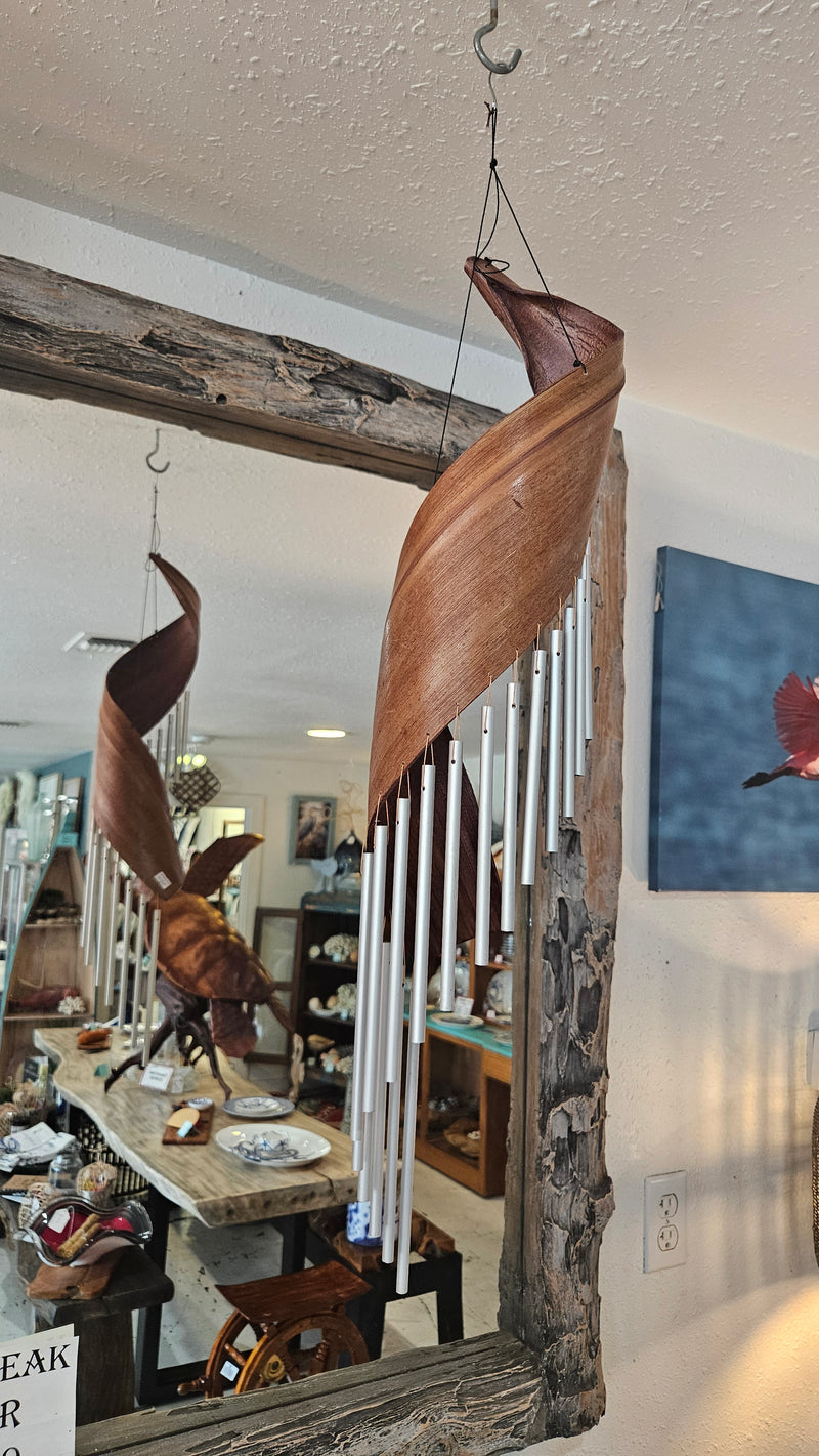 Handcrafted spiral wind chime made from natural palm frond with silver metal chimes, hanging in rustic indoor setting.