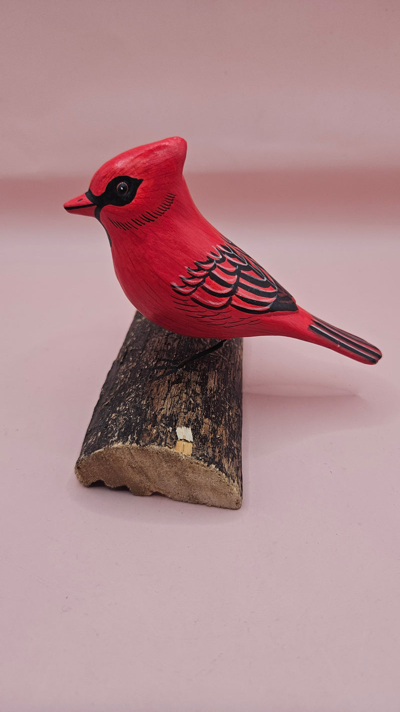 Photo of hand-carved wooden cardinal figurine, painted in bright red with black detailing, perched on a unique natural wood base.