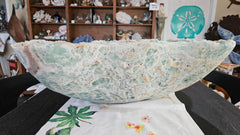 Large carved fluorite crystal bowl with green and translucent veining, displayed on tropical floral fabric
