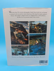 Hardcover of Family Houses by the Sea showing a child reading on a floral daybed inside a green-painted seaside cottage with white trim and sunlit windows.