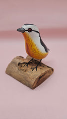 Photo of hand-carved wooden songbird figurine with grey, white, and yellow painted details, perched on a natural driftwood base.