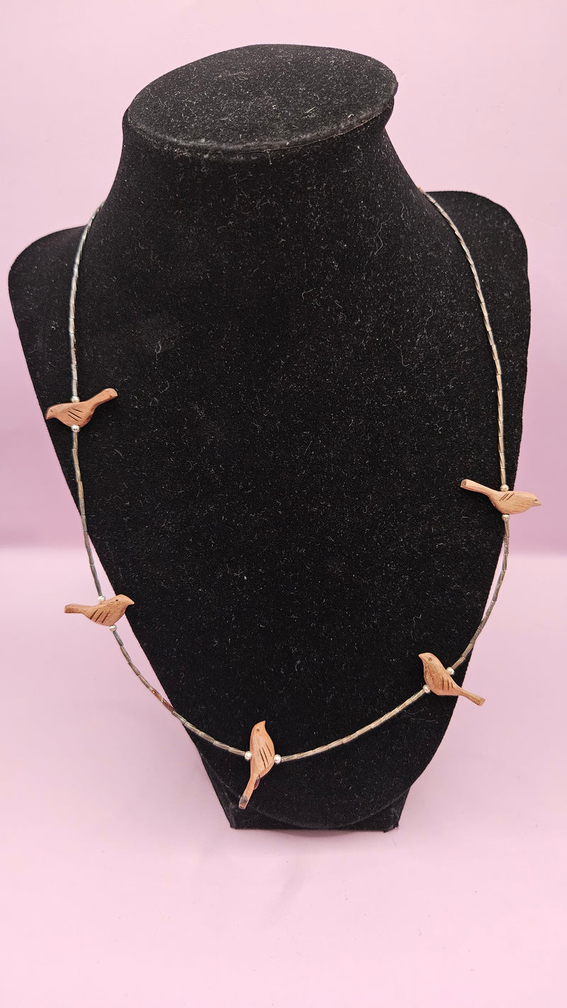 10.5" handmade necklace with carved wooden bird charms and a delicate metallic chain, displayed on a black stand with a pink background.