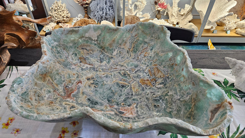 Large carved fluorite crystal bowl with green and translucent veining, displayed on tropical floral fabric
