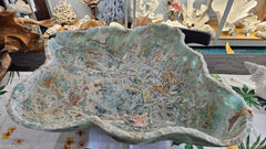 Large carved fluorite crystal bowl with green and translucent veining, displayed on tropical floral fabric