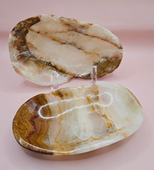 Two earth-tone onyx dishes with natural swirls of tan, cream, and rust on pink background
