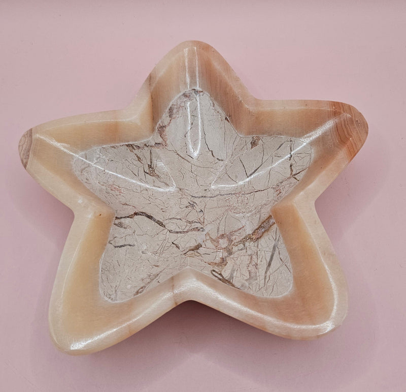 Light pink and ivory polished onyx star-shaped dish with natural veining on pink background