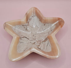 Light pink and ivory polished onyx star-shaped dish with natural veining on pink background