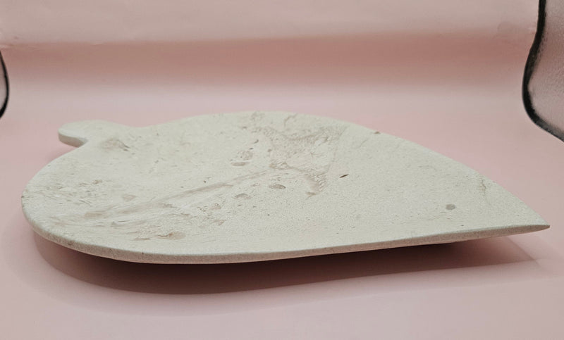 Leaf-shaped fossil marble shallow dish with subtle imprints, shown on a pale pink background.
