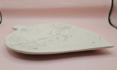 Leaf-shaped fossil marble shallow dish with subtle imprints, shown on a pale pink background.