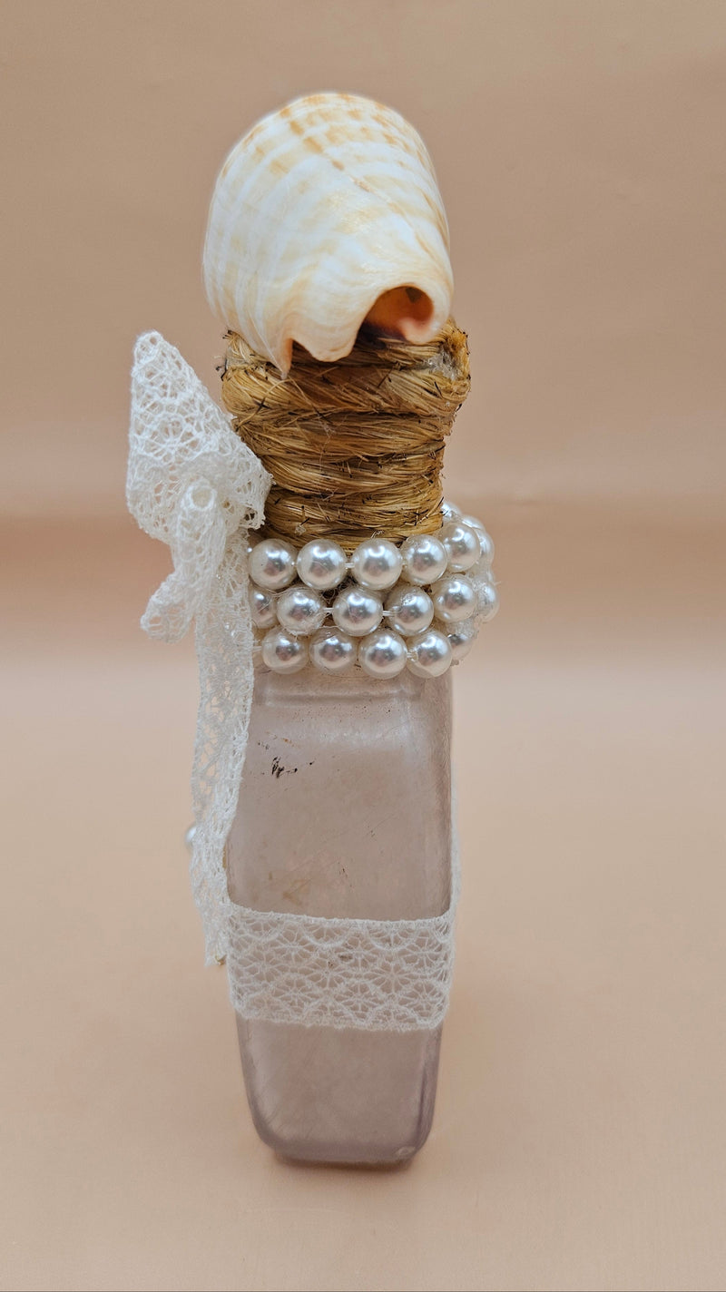 Vintage 5.5"x2" decorative bottle with a spiral seashell top, lace bow, pearl accents, and gold starfish charm against a neutral background