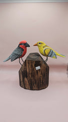 Hand-painted wooden songbird figurines in red/yellow and blue/yellow perched on rustic wood stumps, displayed on a green tabletop.