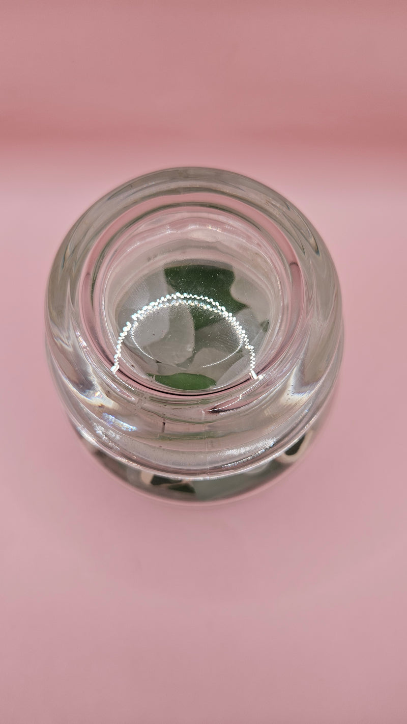 Apothecary glass jar filled with aqua and green sea glass and pottery shards, coastal decor accent on pink background