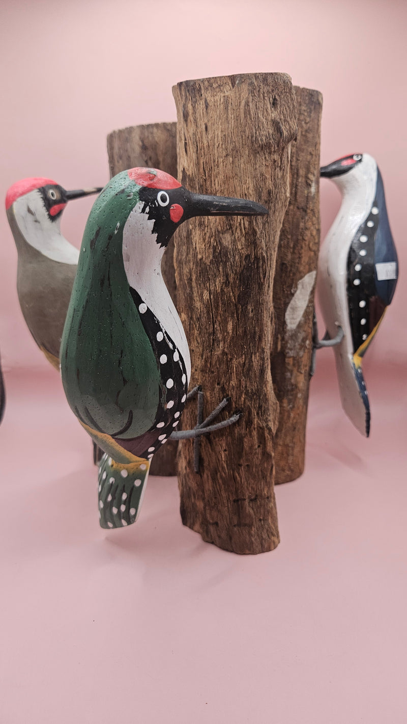 Three individual hand-painted woodpecker figures mounted on varying pieces of natural wood displayed on a teal tabletop.