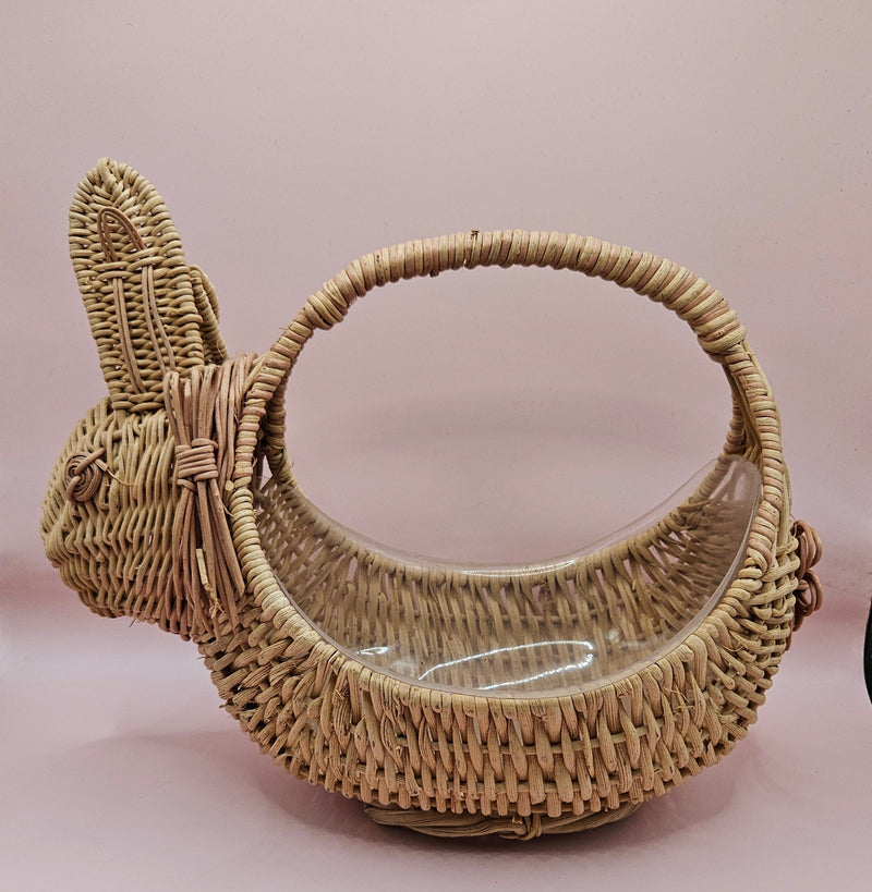 Vintage handwoven wicker basket in the shape of a rabbit with detailed ears and handle, photographed against a pink background.