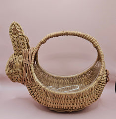 Vintage handwoven wicker basket in the shape of a rabbit with detailed ears and handle, photographed against a pink background.