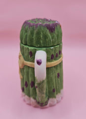 Vintage ceramic miniature teapot shaped like asparagus stalks with purple tips and a yellow ribbon bow, approximately 3.6 inches tall.