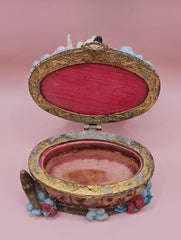Whimsical vintage trinket box featuring a winged angel holding a basket of flowers, a cherub riding a spotted cow, and decorative star details on a round pastel base.