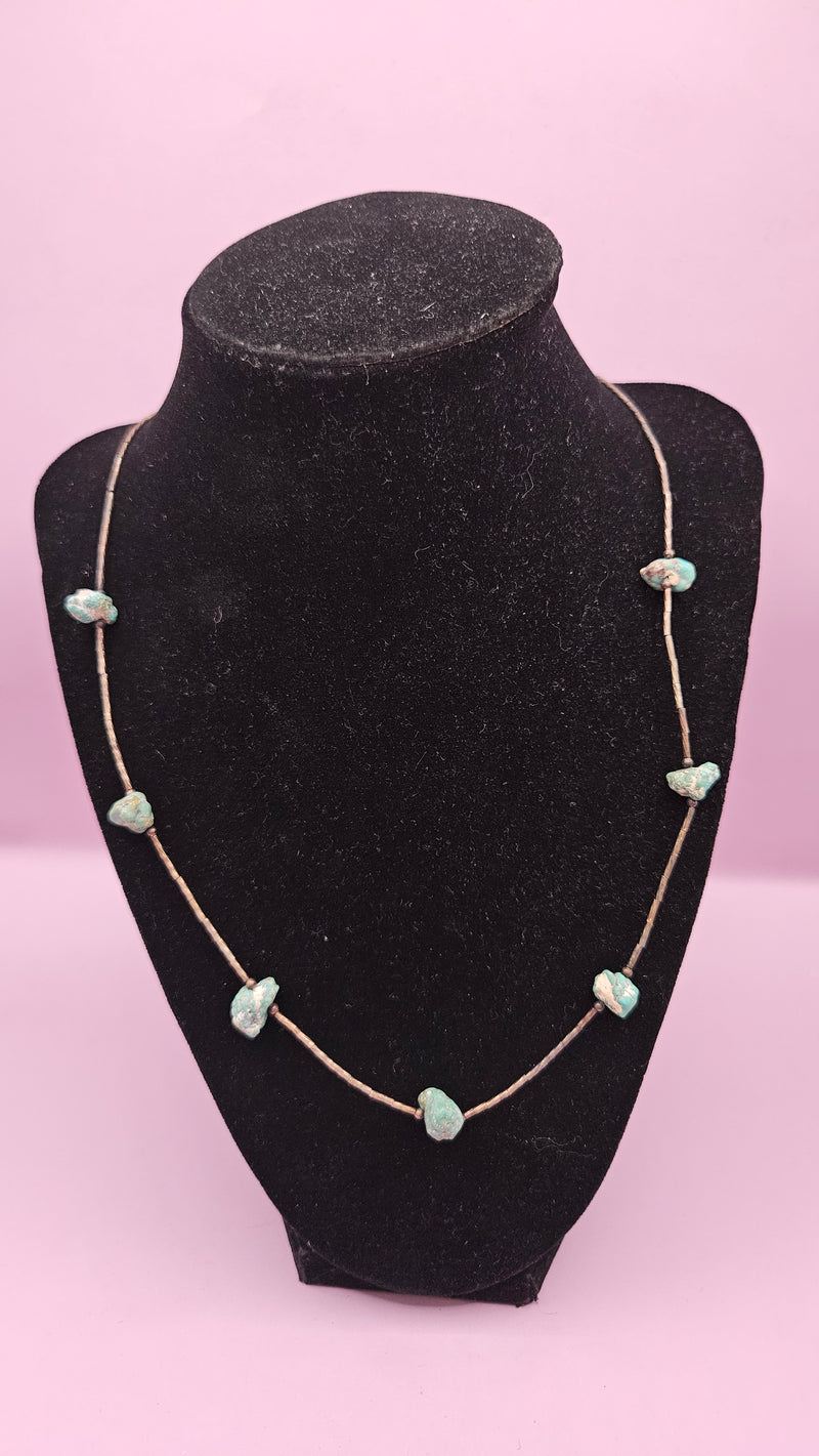 10" handmade turquoise bead necklace featuring small turquoise stones on a delicate metallic chain, displayed on a soft pink background.