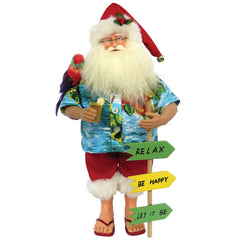 A 15-inch figurine of Santa Claus wearing a blue Hawaiian shirt and red dungarels with a white faux fur trim, holding a drink and with a parrot on his shoulder. He stands on a sandy surface with a sign that has three arrows pointing to 'Relax', 'Be Happy', and 'Let It Be'.