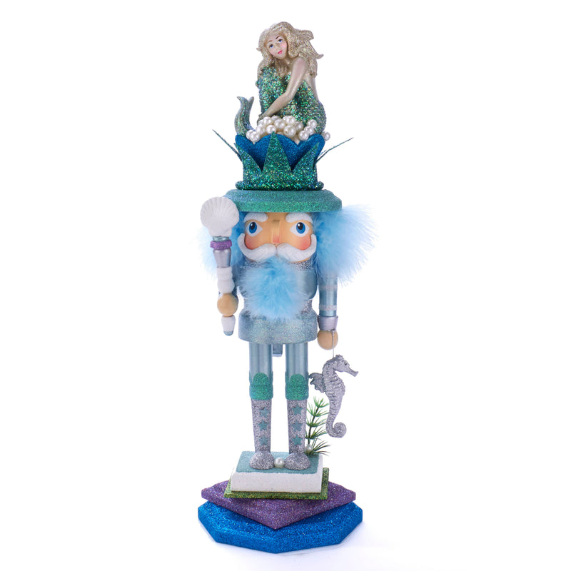 A HOLLYWOOD MERMAID KING NUTCRACKER featuring a seahorse and nautical-inspired design. The nutcracker is decorated with a blue and green mermaid sitting atop a green hat with a purple base, resembling a nautical chart.