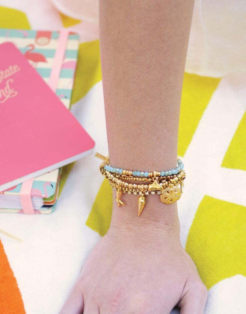 A lifestyle image of the Washed Ashore Beaded Toggle Bracelet styled on a wrist with complementary gold accessories.
